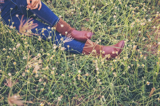 An individual walking barefoot on a grassy field, surrounded by wildflowers under a clear blue sky. The person is smiling and appears relaxed, with their arms slightly outstretched. Focus on the person connecting with nature through touch.