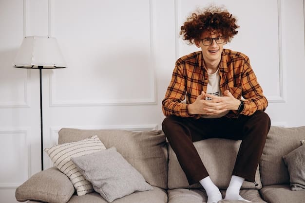 A person comfortably seated on a couch, holding a phone and looking at it with a calm and focused expression. A warm light and comforting setting suggest they are receiving support or guidance through a helpline or teletherapy session.