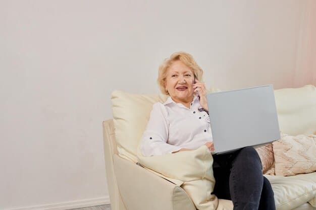 An elderly woman is sitting in a comfortable armchair at home, talking on the phone with a friendly expression. She appears to be discussing her long-term care insurance policy with an insurance agent. Bright natural light fills the room.