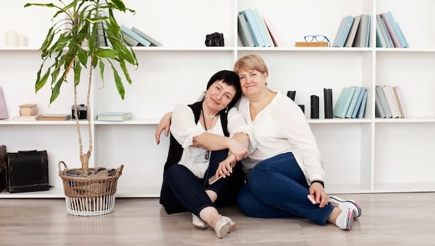 A middle-aged woman, possibly a daughter, is kneeling next to her elderly mother, who is sitting in a comfortable armchair at home. The daughter is holding her mother's hand and looking at her with a concerned expression. The background is a warm, inviting living room, suggesting a safe and caring home environment.