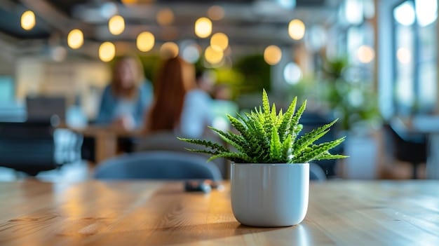 A calm and inviting break room in an office. Soft lighting, comfortable seating, and plants create a relaxing atmosphere. A sign on the wall promotes mental health resources available to employees. A few employees are seen chatting and smiling, enjoying a moment of respite from their work.