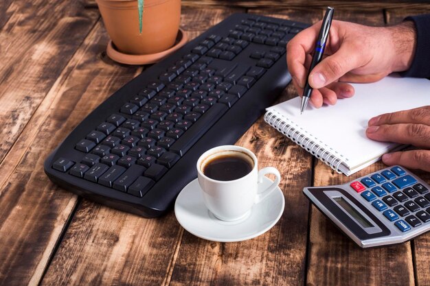 A person is carefully filling out tax forms at a wooden table with a calculator and pen, focusing on details and precision.
