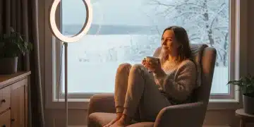 Person using a light therapy lamp by a window in winter.
